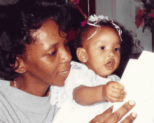 a woman is holding a baby in her arms and the baby is wearing a flower in her hair