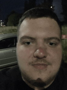 a man with a red nose is standing in front of a car and a no parking sign