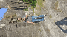 a man in a gray shirt and blue jeans is standing on a rock