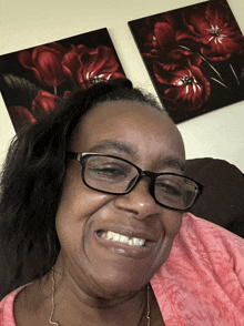 a woman wearing glasses is smiling in front of two paintings of red flowers on the wall