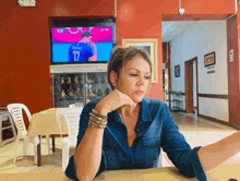 a woman sits at a table in front of a television with a man in a number 17 jersey on it