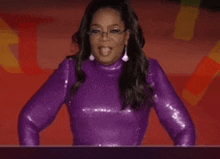 a woman in a purple sequined top and earrings stands in front of a red background