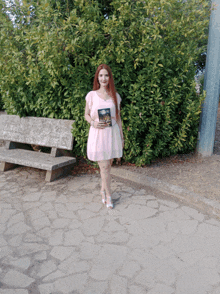 a woman in a pink dress is holding a book in front of a bench