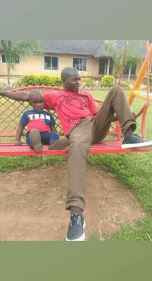 a man in a red shirt is sitting on a red bench with a little boy