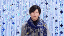 a man wearing a scarf and a sweater is standing in front of a blue background