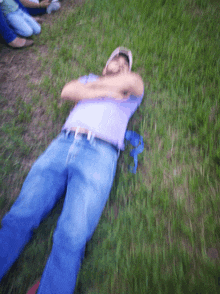 a man in a purple shirt and blue jeans is laying on the grass