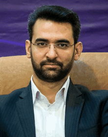 a man with a beard wearing glasses and a suit sits in a chair