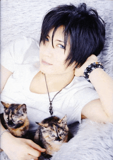 a woman with black hair and blue eyes is laying on a blanket with two kittens