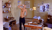 a man without a shirt is drinking from a bottle in a room with a poster that says palantine