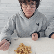 a person wearing a grey sweatshirt with the letter h on it is eating pasta