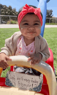 a little girl is sitting on a toy car with a sign that says life isn t easy being a princess