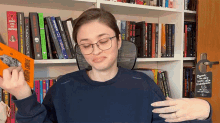 a woman wearing glasses holds a book titled " predator crime " in front of a bookshelf full of books