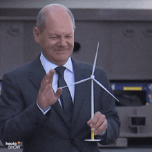 a man in a suit and tie is holding a wind turbine with the words heute show on the bottom right