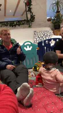 a man is giving a thumbs up while sitting on a couch next to a baby