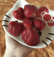 a person is holding a hello kitty plate with strawberries in it