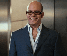 a bald man wearing glasses and a blue suit is smiling