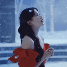 a woman in a red dress is standing in the snow and looking up at the sky .