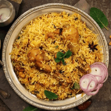 a plate of chicken biryani with onions and mint leaves on a wooden table .