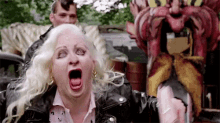 a woman in a leather jacket is making a funny face while standing in front of a carnival ride .