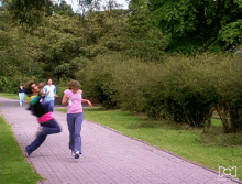 a woman in a pink shirt is running down a path with a man in a blue shirt behind her