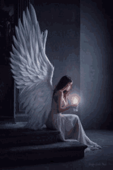 a woman with angel wings is sitting on a set of stairs holding a lit candle .