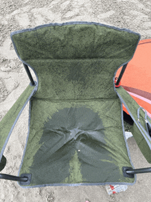 a green folding chair on the beach with a bottle of water next to it