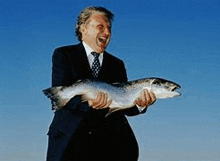 a man in a suit and tie is holding a fish in his hands .