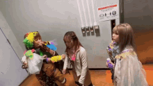 three girls are standing in front of an elevator with a sign on the wall that says ' elevator ' on it