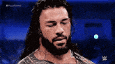 roman reigns is a wrestler with long hair and a beard and is looking down .