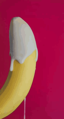 a banana with white icing on it is sitting on a pink surface .