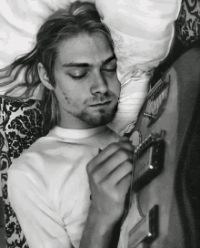 a black and white photo of a man laying on a bed with a guitar