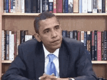 a man in a suit and tie is sitting in front of a bookshelf with a book titled a brief history of america