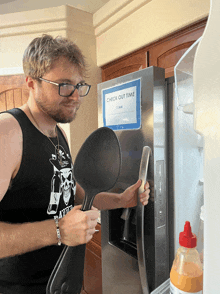 a man holding a spoon in front of a refrigerator that says check out time