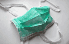 a green surgical mask with white straps on a white surface