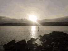 the sun shines brightly over a body of water with rocks in the foreground