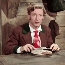 a man in a suit and tie is sitting at a table with a plate of food in front of him