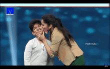 a woman kisses a young boy on the cheek in front of a mallemala tv screen