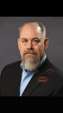 a man with a beard is wearing a black suit and blue shirt