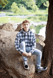 a young man is sitting under a tree on a rock .