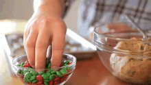 a person 's hand is reaching into a glass bowl filled with green and red m & m 's .