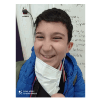 a boy wearing a face mask is smiling in front of a white board that says ' spag ' on it