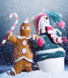 a gingerbread man holding a candy cane next to a snowman in the snow