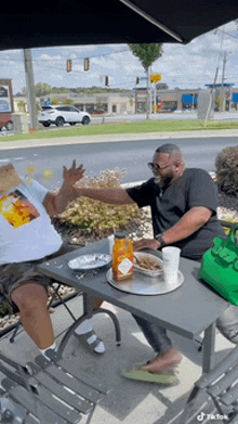 two men are sitting at a table with plates of food and drinks .