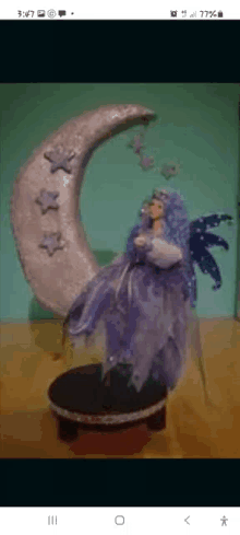 a statue of a fairy sitting on a crescent moon on a wooden table .