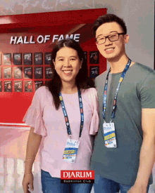 a man and a woman are posing for a photo in front of a wall that says hall of fame