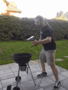 a man in a black shirt that says ' rage ' on it is holding a hair dryer in front of a grill