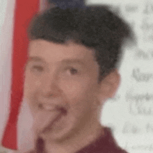 a young boy is sticking his tongue out in front of a flag .