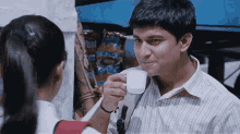 a man is drinking from a white cup while talking to a girl in front of a bag of royal spice