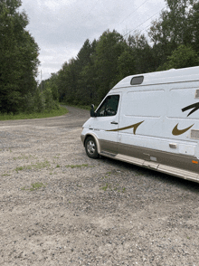 a white van with a gold arrow on the side is parked on a gravel road