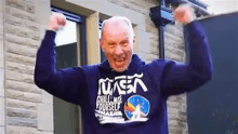 an elderly man wearing a nasa sweatshirt is flexing his muscles .